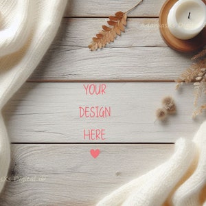 May include: A neutral-toned flat lay with a white wooden surface, a cream-coloured knitted blanket, and a lit candle in a wooden holder. Dried leaves and the text "YOUR DESIGN HERE" add to the warm, inviting aesthetic. A ball of yarn is also visible.