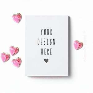 May include: A white card with the text "YOUR DESIGN HERE" and a small black heart. The card is surrounded by pink heart-shaped cookies with white icing and a pink bow.