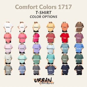 Op de afbeelding: Een display van Comfort Colors 1717 t-shirts in verschillende kleuren, waaronder wit, ivoor, banaan en mosterd. Andere kleuren zijn watermeloen, grunchberry en karmozijnrood. Het Urban Cotton Apparel-logo staat onderaan.