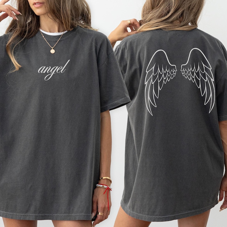 Op de afbeelding: Donkergrijs t-shirt met het woord "angel" in cursiefschrift op de voorkant. De achterkant van het shirt heeft een wit vleugelontwerp. Het shirt is een casual, oversized stijl.