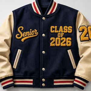 Può includere: Una giacca varsity blu navy con maniche color crema, caratterizzata da ricami gialli con la scritta Senior e Class of 2026, e il numero 26 sulla manica sinistra. La giacca presenta una chiusura con bottoni a pressione, bordi a righe e due tasche.
