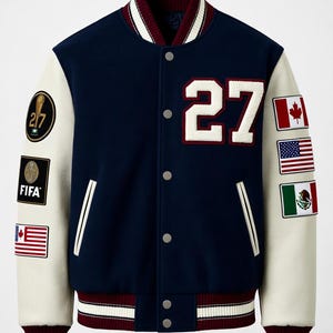 May include: A navy blue varsity jacket with cream-coloured sleeves, featuring the number 27 in white on the chest. The sleeves are adorned with various patches, including the FIFA logo, a trophy graphic, and the flags of Canada, the USA, and Mexico.