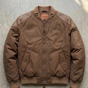 Può includere: Giacca bomber marrone con zip, due tasche frontali e colletto e polsini a coste. La giacca ha inserti in pelle sulle spalle e una piccola etichetta con la scritta "SEEMIGIFT".