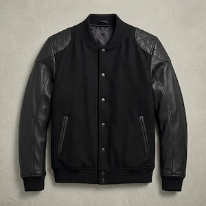 Puede incluir: Chaqueta universitaria negra con mangas de cuero y parches acolchados en los hombros. La chaqueta tiene cuello, puños y dobladillo de canalé, y presenta una parte delantera abotonada y dos bolsillos delanteros.