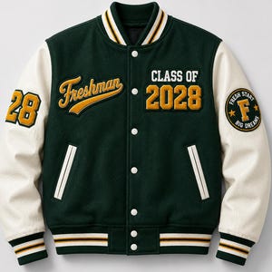 Könnte beinhalten: Eine dunkelgrüne Collegejacke mit cremefarbenen Ärmeln, weißen Druckknöpfen und gestreiften Rippbündchen. Auf der Brust befindet sich ein gelber Stickschriftzug mit Freshman und Class of 2028 sowie ein rundes Abzeichen am Ärmel.