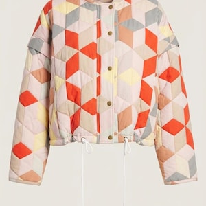 May include: A quilted bomber jacket featuring a geometric pattern of cubes in shades of orange, light pink, yellow, and grey. The jacket has a stand-up collar, a front snap-button closure, long sleeves, and a drawstring hem with white cords.