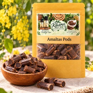 Peut inclure: Un sachet beige étiqueté Kshama Handcrafted Amaltas Pods contenant des segments végétaux cylindriques brun foncé. Un bol en bois rempli de segments identiques brun foncé est placé devant, avec deux segments posés sur la surface texturée.