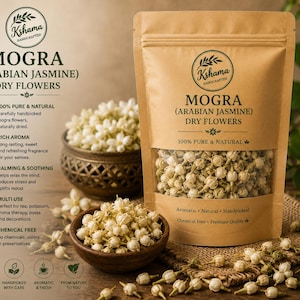 Op de afbeelding: Een bruine papieren zak met het label Mogra Arabian Jasmine dry flowers met gedroogde witte bloemknoppen. De verpakking bevat het Kshama Handcrafted logo, tekst over 100% natuurlijke ingrediënten en een doorzichtig venster voor de inhoud.