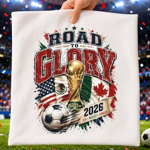 May include: A white square pillow featuring a graphic print with the text ROAD TO GLORY, a gold FIFA World Cup trophy, a soccer ball, and the flags of the USA, Mexico, and Canada, with the text 2026 USA MEXICO CANADA on a banner.