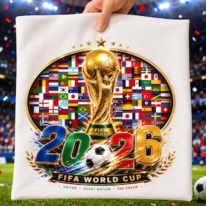 May include: A white square pillow featuring a gold FIFA World Cup trophy centered within an oval frame of international flags. Below, the text 20-26 appears in large metallic numbers with a soccer ball, followed by FIFA WORLD CUP UNITED EVERY NATION ONE DREAM.