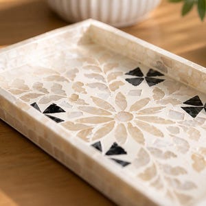 May include: Rectangular decorative tray with a mosaic floral design. The tray features a cream-colored background with a flower and leaf pattern in beige and black. The edges are also cream-colored and tiled.