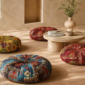 May include: Three round floor cushions featuring intricate, multi-colored patterns in shades of red, blue, yellow, and green. Each cushion has a tufted center and a plush, circular shape, arranged on a light-colored floor near a low wooden table.