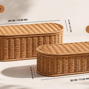 May include: Two woven wicker storage baskets, one large and one small, with oval shapes and lids. The larger basket is 38 cm (14.96 inches) long, 14 cm (5.51 inches) wide, and 9 cm (3.54 inches) high. The smaller basket is 28 cm (11.02 inches) long.