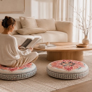 May include: Two round floor cushions featuring a central mandala pattern in shades of pink, orange, and teal on a cream background. The sides of the cushions are decorated with a detailed black and white geometric border print on a white fabric base.