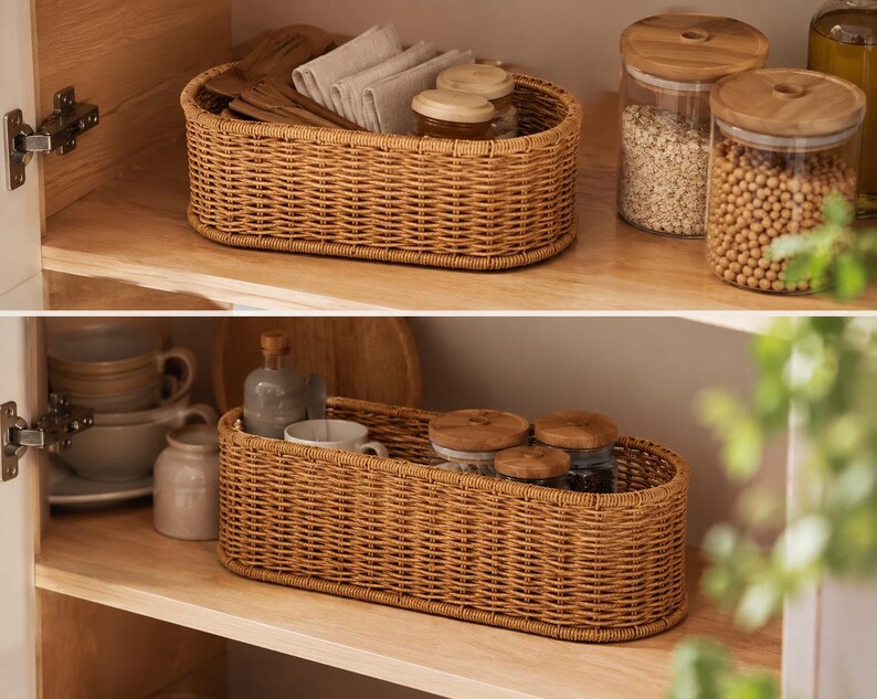May include: Two wicker baskets, one on each shelf, filled with kitchen items. The top basket holds wooden utensils and folded linen napkins. The bottom basket contains mugs and small jars. Glass jars with wooden lids are also visible.
