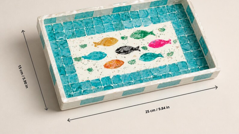 May include: Rectangular decorative tray with a mosaic tile border and a central design of colorful fish. The tray measures 9.84 inches long and 5.90 inches wide. The fish are in shades of yellow, green, pink, black, blue, and orange.
