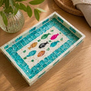 May include: Rectangular decorative tray with a mosaic tile border in shades of turquoise and white. The tray's center features colorful fish illustrations in orange, pink, green, and black. A stylish accent piece for home decor.