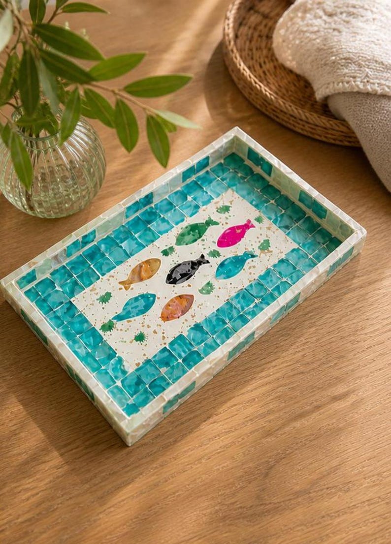 May include: Rectangular decorative tray with a mosaic tile border in shades of turquoise and white. The tray's center features colorful fish illustrations in orange, pink, green, and black. A stylish accent piece for home decor.