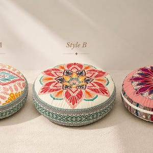May include: Three round floor cushions labeled Style A, Style B, and Style C. Style A features a teal, pink, and yellow floral pattern. Style B has a red, orange, and yellow mandala design on cream. Style C displays a purple and pink floral motif.