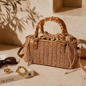 Peut inclure: Un sac à main rectangulaire en paille tressée doté d'une anse en bambou marron clair, d'une fermeture à cordon en tissu beige et d'une bandoulière fine en cuir marron amovible. Le sac possède une base structurée et des détails en métal doré.