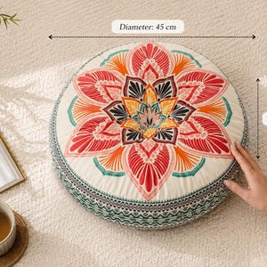 May include: A round floor cushion featuring a vibrant, multi-colored mandala pattern in shades of red, orange, yellow, and teal on an off-white background. The cushion has a diameter of 17.7 inches and a thickness of 3.1 inches as labeled.