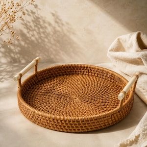 Peut inclure: Un plateau rond en rotin tressé, de couleur marron clair. Il est équipé de deux poignées en bois clair. Le motif tressé forme une spirale au centre. Ce plateau est conçu pour le service ou la présentation.