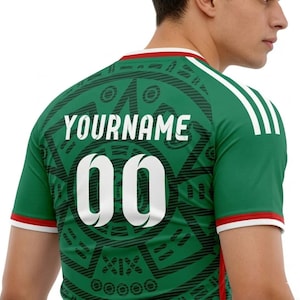 Puede incluir: Camiseta de f&uacute;tbol verde con detalles blancos, con el texto "YOURNAME" sobre el n&uacute;mero "00" en blanco. La camiseta tiene un dise&ntilde;o estampado en la espalda y rayas blancas en los hombros.
