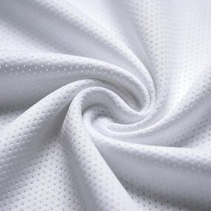 Puede incluir: Primer plano de tela blanca transpirable con una superficie texturizada y perforada. El material est&aacute; tejido apretado, con un brillo sutil, y est&aacute; dispuesto en pliegues y curvas suaves. La tela parece ligera y adecuada para ropa deportiva.