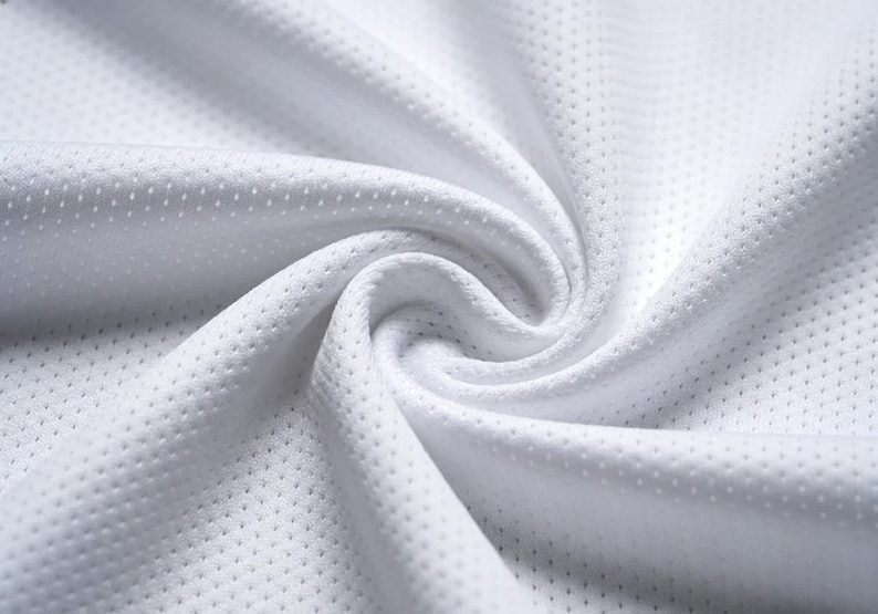 Puede incluir: Primer plano de tela blanca transpirable con una superficie texturizada y perforada. El material est&aacute; tejido apretado, con un brillo sutil, y est&aacute; dispuesto en pliegues y curvas suaves. La tela parece ligera y adecuada para ropa deportiva.