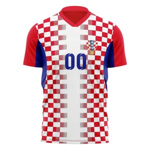 May include: A red, white, and blue soccer jersey with the number "00" on the front. The jersey features a checkered pattern on the front and sleeves, with a Croatian emblem on the chest. The sleeves are red, and the collar is a V-neck.