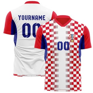 May include: A white and red checkered soccer jersey with blue accents and the number "00". The jersey has a V-neck collar and the Croatian coat of arms. The back of the jersey has the name "YOURNAME" and the number "00".