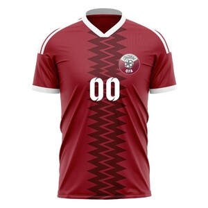 Puede incluir: Camiseta de f&uacute;tbol granate con detalles blancos, que presenta un dise&ntilde;o en zigzag en la parte delantera. La camiseta tiene el n&uacute;mero "00" en blanco y un emblema circular en el pecho. Las mangas tienen rayas blancas.