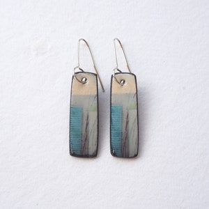 May include: A pair of silver dangle earrings with rectangular ceramic charms. The charms are decorated with an abstract design in blue, white and brown.