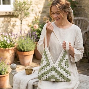 May include: A handmade crochet tote bag featuring a classic granny square pattern in alternating sage green and off-white yarn. The bag has a triangular shape with a single integrated shoulder strap and a textured, open-work stitch construction.