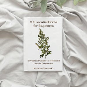 Op de afbeelding: Een wit boek met de titel "10 Essential Herbs for Beginners" met een botanische illustratie. Het boek bevat ook de tekst "A Practical Guide to Medicinal Uses & Properties" en de merknaam "HerbsAndMortarCo".