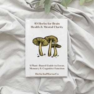 May include: A white book with the title "10 Herbs for Brain Health & Mental Clarity" and a mushroom illustration. The book also reads "A Plant-Based Guide to Focus, Memory & Cognitive Function" and "HerbsAndMortarCo".