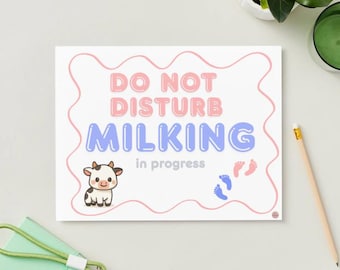 May include: A white sign with the words "DO NOT DISTURB MILKING in progress" in pink and blue bubble letters. A cartoon cow and footprints are also on the sign. A pencil and a green notebook are in the background.