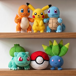 Puede incluir: Una colección de personajes Pokémon hechos a mano con ganchillo, incluyendo Charmander, Pikachu, Squirtle, Bulbasaur, una Poké Ball y una criatura azul con hojas verdes. Los juguetes se exhiben en estantes de madera, mostrando colores vibrantes y artesanía detallada.