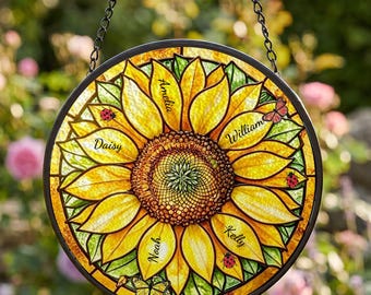 Puede incluir: Un atrapasoles circular de vidriera con un gran girasol amarillo y hojas verdes. Los pétalos llevan inscritos los nombres Amelia, William, Kelly, Noah y Daisy. En el cristal aparecen pequeñas mariquitas y una mariposa.