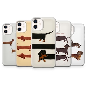 May include: A collection of five phone cases featuring dachshund dog illustrations. The cases display various designs, including solid-colored dogs, striped backgrounds, and the text "GOOD DOGS". The cases are in a variety of colors, including tan, black, and brown.
