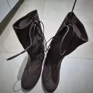 May include: A pair of dark brown mid-calf boots featuring a lace-up front design with matching dark brown laces. The boots have a rounded toe, a structured shaft that reaches the mid-calf, and a smooth finish throughout the exterior surface.