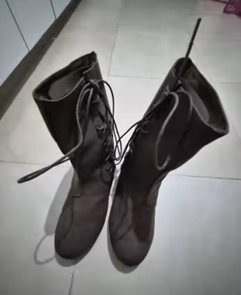 May include: A pair of dark brown mid-calf boots featuring a lace-up front design with matching dark brown laces. The boots have a rounded toe, a structured shaft that reaches the mid-calf, and a smooth finish throughout the exterior surface.