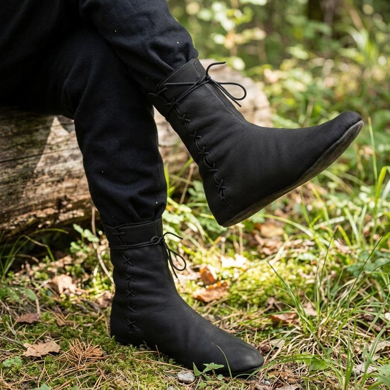 May include: A pair of black mid-calf boots featuring a smooth matte finish, rounded toes, and a decorative lace-up design that runs vertically along the outer side of each boot, secured with thin black laces tied at the top of the shaft.