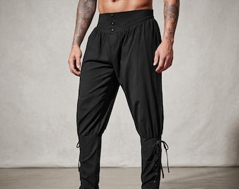 May include: Black trousers featuring a high-waisted design with three front buttons, a loose-fitting upper section, and fitted lower legs that include side lacing details. The fabric has a matte finish and the pants reach the lower calf area.