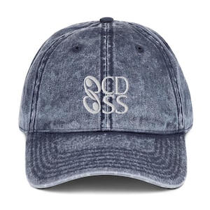 Puede incluir: Gorra de béisbol azul vaquero con visera curva. La gorra presenta el texto bordado "OCD SSS" en hilo blanco en la parte delantera. El sombrero tiene un aspecto desgastado y vintage.