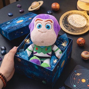 May include: A Buzz Lightyear soft toy presented in a space-themed gift box. The toy features a purple head, green and white spacesuit, and blue eyes. The box is decorated with planets and stars. Other space-themed items are in the background.
