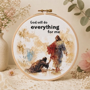 May include: A circular wooden embroidery hoop containing a cross-stitch artwork depicting a figure kneeling before a standing figure in a red and blue robe. The text "God will do everything for me" is stitched in black at the top of the fabric.