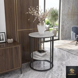 May include: A modern side table with a white marble top and a black metal frame. The table has two shelves and a decorative gold geometric sculpture. A white vase with flowers sits on top. The table is 24 inches in diameter.