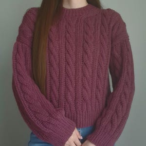 May include: A white ceramic mug with a black handle and the text "But First, Coffee" in a handwritten style. The mug is on a white surface. The mug is approximately 10 cm tall.