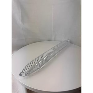 May include: A long, narrow, clear glass dish featuring a repeating vertical ribbed pattern along its sides. The dish has a pointed, tapered shape at both ends and a smooth, rounded base, creating a sleek, elongated form made of transparent glass.